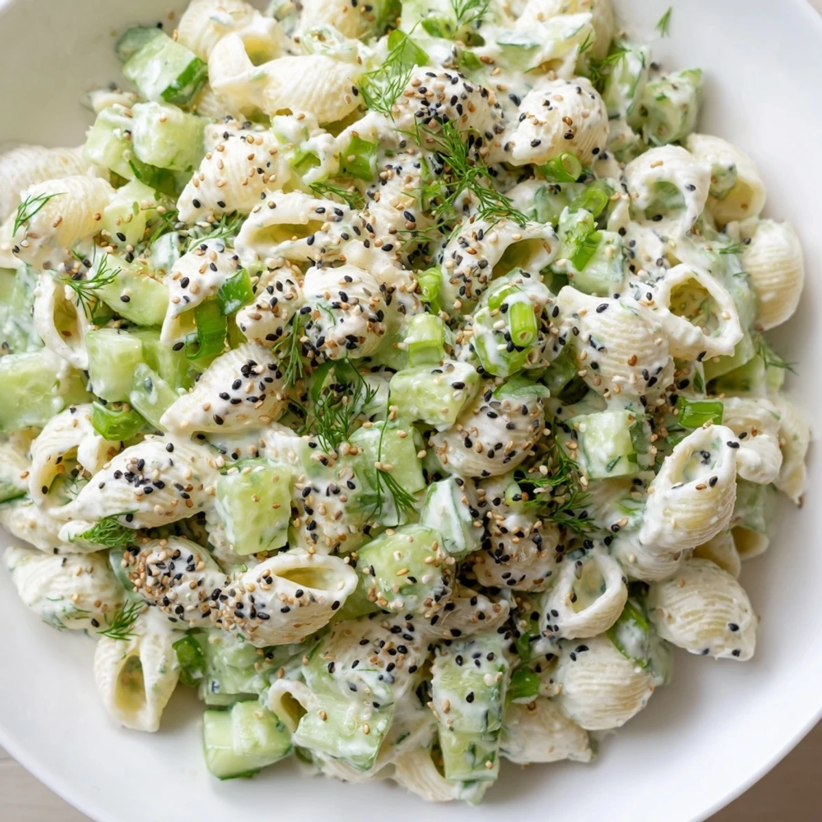 A bowl of vegetarian Cucumber Crunch Pasta Salad with crunchy cucumbers, aromatic dill, and savory everything bagel seasoning on a picnic-ready table setting.
