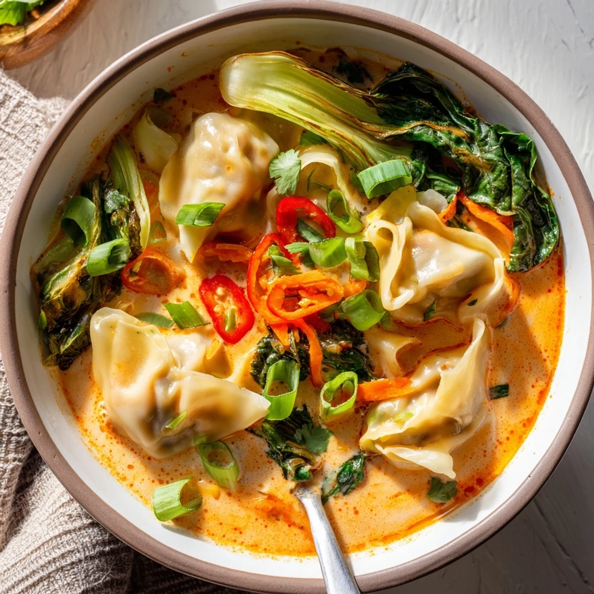 Steaming bowl of Red Curry Wonton Soup with baby spinach and fresh lime wedges.