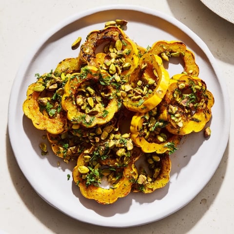Golden-brown baked delicata squash rings, drizzled with maple syrup and sprinkled with pistachios.