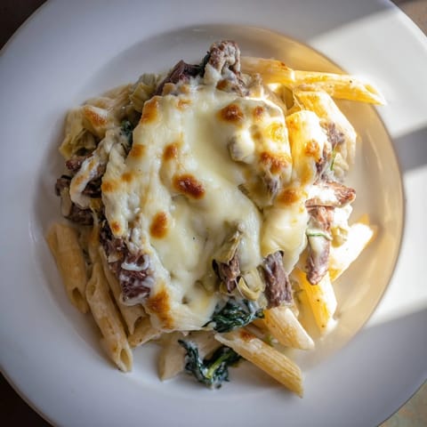 A steaming close-up of Steak & Spinach Artichoke Pasta Bake, highlighting the tender beef and creamy sauce.