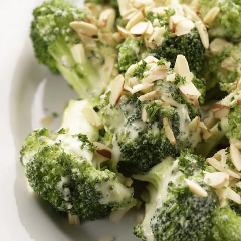 Garlic Parmesan Broccoli Salad served in a white bowl with red onion slices and cherry tomatoes.