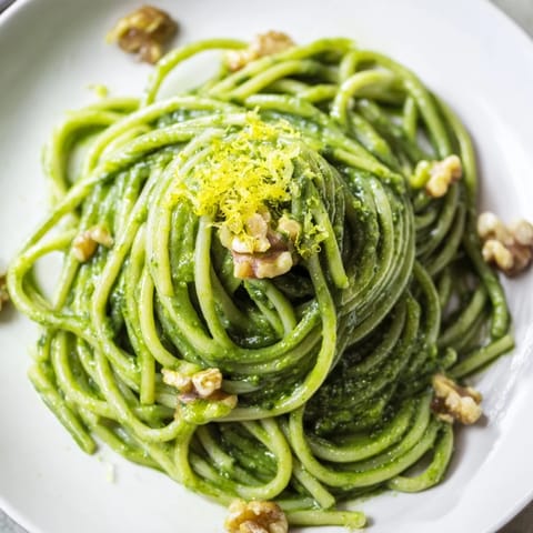 Perfectly coated creamy spinach walnut pasta in a velvety green sauce, garnished with chopped walnuts and served alongside a crisp green salad.