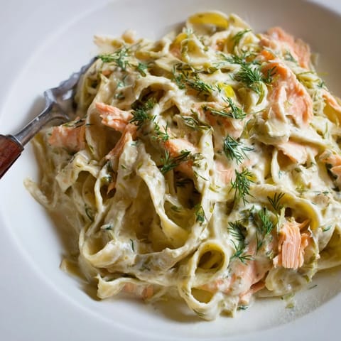 Steaming creamy salmon pasta on a dinner plate, featuring hot-smoked salmon flakes, lemon zest, and grated Parmesan topping.